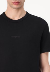 Must mustriba puuvillane T-särk, millel on ümmargune kaelus ja lühikesed varrukad. Rinnal on tagasihoidlik "tommy jeans" logo brodering.