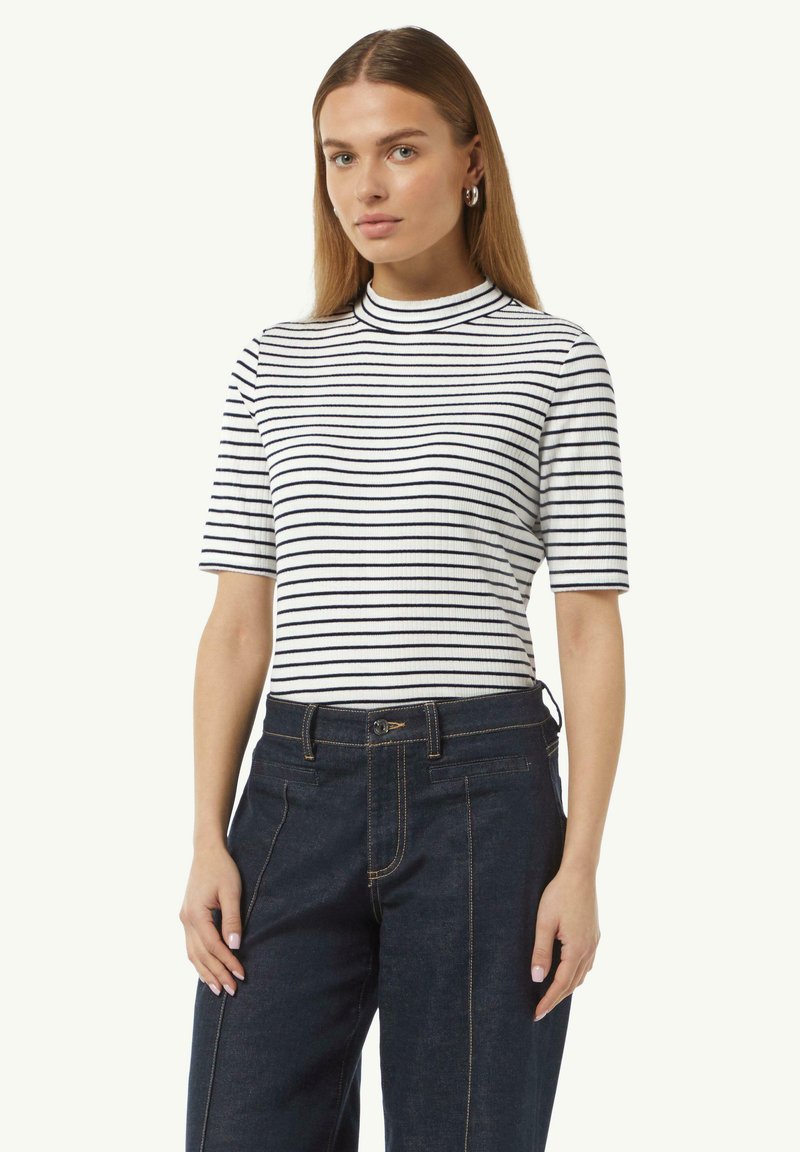 Weißes und marineblau gestreiftes Kurzarmoberteil mit hohem Kragen; weicher, gerippter Stoff; kombiniert mit dunkelblauen, maßgeschneiderten Jeans.
