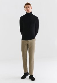 Czarny sweter z golfem, dopasowany krój, gładki materiał; w zestawieniu z jasnobeżowymi spodniami, slim fit, subtelna tekstura; czarne botki za kostkę.