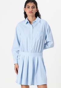 Vestido camisa riscas azuis claras com mangas longas, colarinho, um bolso frontal e uma cintura elástica, apresentando um design de saia plissada.