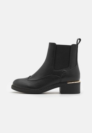 Bottine en cuir noir avec panneau latéral élastique, languette à l'arrière, petit talon superposé et accent doré près du talon.