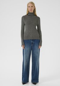 Maglione grigio a coste con collo alto e vestibilità aderente, con maniche lunghe, abbinato a jeans a gamba larga blu e scarpe nere a punta.