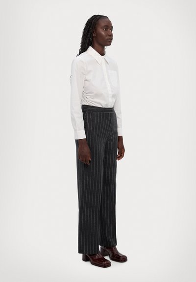 White button-up shirt with a pocket, paired with dark gray pinstripe trousers and glossy burgundy heeled shoes. Smooth texture, tailored fit.