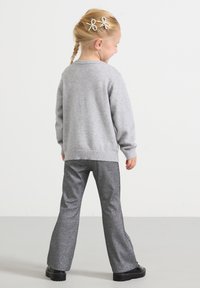 Camisola cinzenta tricotada com bainha canelada, combinada com calças cinzentas cintilantes e flare. Cabelo da criança decorado com laços.