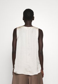 Top senza maniche in seta color crema con una finitura leggermente textured, caratterizzato da un collo rotondo e una vestibilità rilassata. Nessun hardware o motivo visibile.