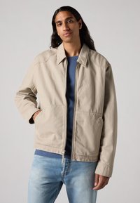 Bežna zip-up jakna iz bombaža, z ravnim ovratnikom, stranskimi žepi in udobnim krojem. V kombinacji z modro srajco in svetlimi jeans.