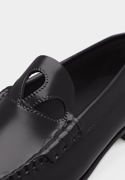 Mocassin en cuir noir avec des détails découpés et des coutures décoratives sur la tige, présentant une finition lisse et brillante ainsi qu'un bout arrondi.