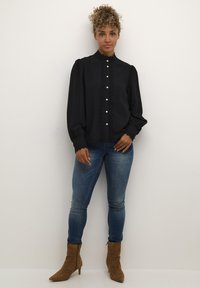 Black blouse with lace detailing down the front, high collar, and button closure. Paired with blue jeans and brown ankle boots.