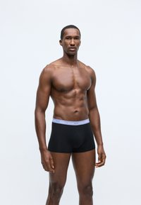 Μαύρα μποξεράκια φτιαγμένα από μαλακό υλικό, με ανοιχτό μωβ ζωνάκι που έχει το λογότυπο "BJÖRN BORG". Το μοντέλο στέκεται με τα χέρια χαλαρά.