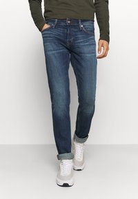 Mörkblå denimjeans med smal passform, med orange sömmar, främre fickor och uppvikta muddar. Kombinerade med ljusa sneakers.