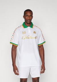 T-shirt polo blanc avec col vert et accents orange. Monte un texte doré "Authentique" et le numéro "10". Patron à rayures sur les manches.