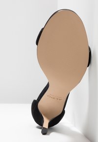 Chaussure noire à talon haut montrant une semelle lisse couleur cuir clair avec le nom de la marque ALDO et une zone texturée pour l'adhérence.