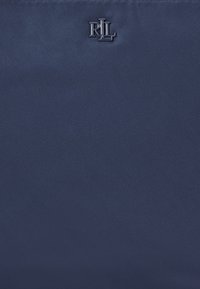 Textilväska i marinblått med texturerad yta; har en silverfärgad logotyp "R.L." präglad i mitten. Enkel, rektangulär form.