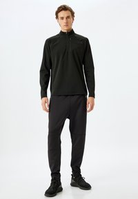 Sudadera negra deportiva de media cremallera con mangas raglán, combinada con pantalones de chándal negros ajustados que cuentan con bolsillos con cremallera y un acabado mate.
