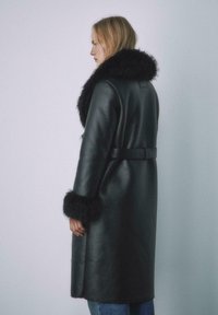 Czarny skórzany płaszcz o fakturowanej powierzchni, z puszystym czarnym futrzanym kołnierzem i mankietami oraz paskiem wiązanym w talii.