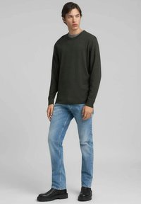 Donkergroene trui van een zachte brei, ronde hals, gecombineerd met lichtblauwe spijkerbroek en zwarte enkellaarsjes. Eenvoudig ontwerp zonder patronen.