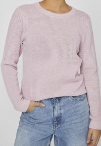 Ljust rosa stickad tröja med rund halsringning, långa ärmar och ribbade muddar, kombinerad med ljusblå denimjeans. Texturerad tyg.