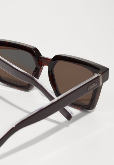 Square-frame sunglasses with dark brown tinted lenses, made from glossy brown plastic, featuring thin, angular arms and a silver accent.
