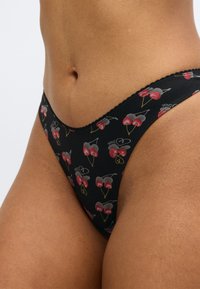 Mustad tangadeta aluspüksid, millel on kirsiembleem punases, hallis ja kollases värvitoonis, laineliste servadega ja pehme ning veniva tekstuuriga.