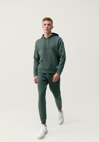 Tmavohnedá mikina s kapucňou a zodpovedajúce tepláky z mäkkej látky, s prednou klokankou a rebrovanými manžetami, skombinované s bielymi teniskami.