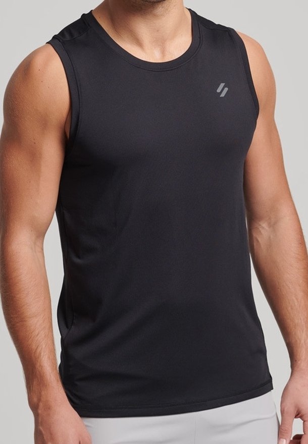 Personne musclée portant un débardeur noir de sport avec un petit logo sur la partie supérieure gauche de la poitrine et un short de couleur claire.