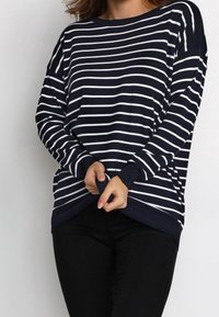 Marineblau und weiß gestreifter Pullover mit lockerer Passform, rundem Ausschnitt und langen Ärmeln. Rippstrickbündchen und Saum. Kombiniert mit schwarzen Hosen.