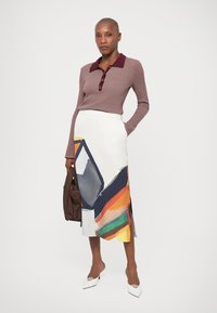 Burgundi bordázott, hosszú ujjú felső gombokkal, fehér szoknyával párosítva, mely nagy, absztrakt, sokszínű mintákkal díszített, valamint hegyes fehér cipőkkel.