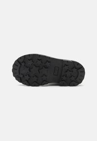 Czarna gumowa podeszwa buta z gwiazdkowymi bieżnikami i gładką częścią środkową. Posiada logo na boku, zaprojektowana z myślą o przyczepności i trwałości.