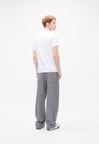 White short-sleeve t-shirt and gray wide-leg sweatpants. T-shirt is smooth, pants are soft with two back pockets. Model is shown from behind.