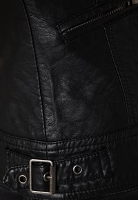 Svart läderjacka med texturerad yta, silverfärgade spännen och en ficka med dragkedja.