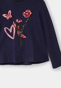 Námornická košile s dlouhým rukávem, na které je vyšitý růžový srdce, červené a růžové květiny a červená a bílá flitrová motýl na přední straně.