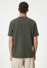 Olivenfarvet t-shirt med korte ærmer og ribbet tekstur samt et klassisk rundhalsdesign, vist fra ryggen.