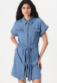 Denim srajčna obleka v svetlo modri barvi, kratki rokavi, gumbno zapiranje spredaj, dve žepu na prsih in pas, ki se zaveže. Gladka tekstura, dolžina do kolen.