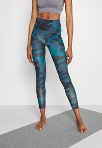 Legíny s vysokým pasem v tyrkysovém a šedém maskovacím vzoru s hladkým povrchem. Mají plochý pas a přiléhavý střih.