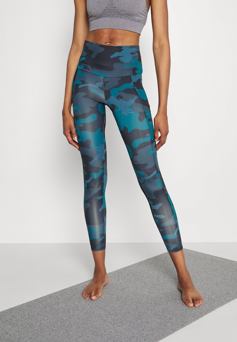 Legíny s vysokým pasem v tyrkysovém a šedém maskovacím vzoru s hladkým povrchem. Mají plochý pas a přiléhavý střih.