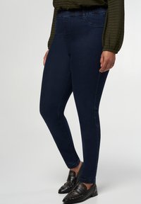 Leggings en denim bleu foncé avec une coupe slim, dotés d'une taille élastique et sans matériel ou embellissements visibles. Accentué par des mocassins noirs.