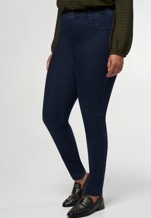 Leggings en denim bleu foncé avec une coupe slim, dotés d'une taille élastique et sans matériel ou embellissements visibles. Accentué par des mocassins noirs.