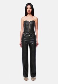 Schwarzes Leder-Korsettoberteil mit vorderer Schnürung, kombiniert mit locker sitzenden schwarzen Lederhosen. Glatte Textur, minimalistisches Design.