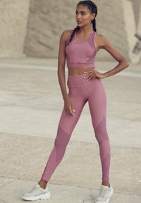 Light purple athletic set with a fitted sports bra and high-waisted leggings. Features textured accents and a seamless design. Footwear is white.