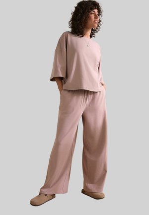 Světle růžové oversized tričko s širokými rukávy, spárované s volnými kalhotami ve stejné barvě. Měkká textilie, elastický pas.