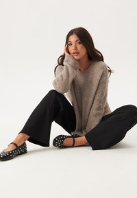 Maglione fuzzy marrone chiaro con vestibilità morbida, abbinato a pantaloni neri a gamba larga. Calzature con ballerine nere con pois bianchi.