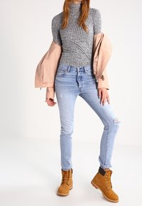Blusa de manga larga gris con estampado, chaqueta rosa clara, jeans desgastados de color azul claro y botas de cordones color marrón claro con suela gruesa.