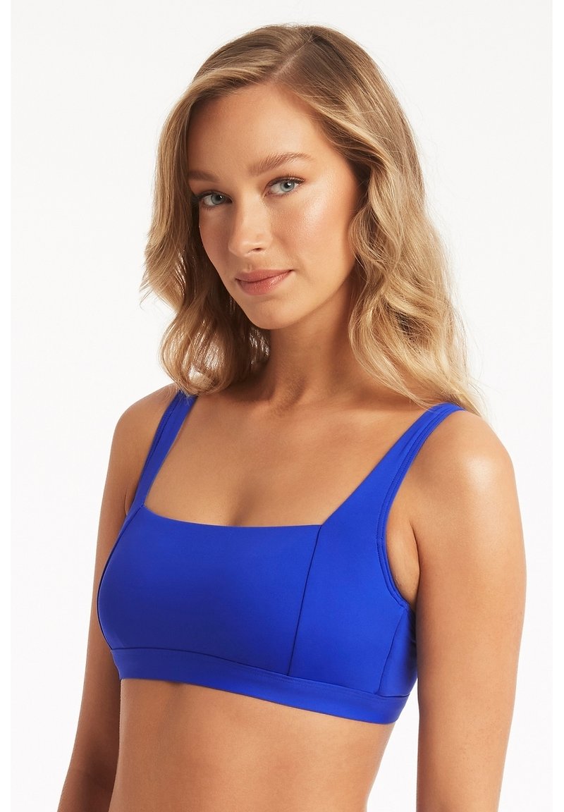 Niebieski stanik sportowy z gładkiego, rozciągliwego materiału. Posiada kwadratowy dekolt, szerokie ramiączka oraz minimalne szwy dla komfortu i wsparcia.