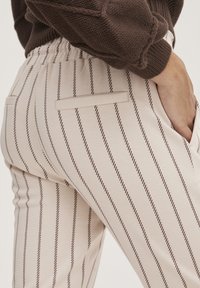 Beige randiga byxor med en mjuk textur, som har tunna bruna vertikala ränder, elastisk midja och två bakfickor.