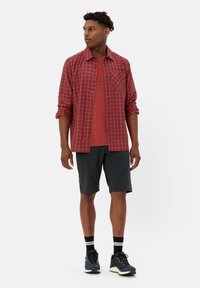 Rood-wit geblokt overhemd met knopen over een rode T-shirt, gecombineerd met zwarte shorts en donkere sneakers met accenten.