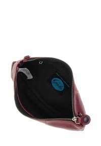 Interno di borsa in pelle rossa con fodera nera, chiusura con zip e etichetta logo in rilievo. Esterno texturizzato e dettagli della zip lisci.