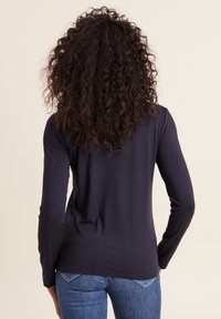 Marineblaues Langarmoberteil aus weichem Stoff, mit taillierter Passform und rundem Ausschnitt, kombiniert mit blauen Jeans. Keine sichtbaren Muster oder Akzente.