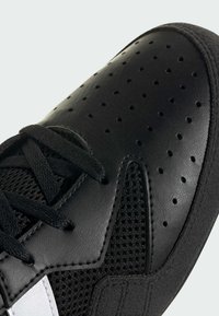 Gros plan sur la pointe d'une basket noire en cuir perforé, panneaux en mesh, lacets noirs et accent blanc sur une semelle texturée.