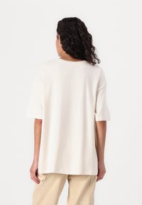 T-shirt surdimensionné couleur crème avec des manches courtes, un col rond et en coton, associé à un pantalon en velours côtelé beige clair.