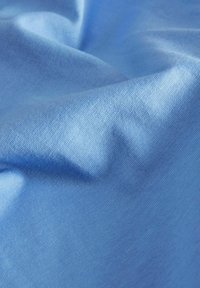 Tessuto azzurro chiaro con una texture liscia, leggermente stropicciato, caratterizzato da un motivo a maglia fine e un colore uniforme.